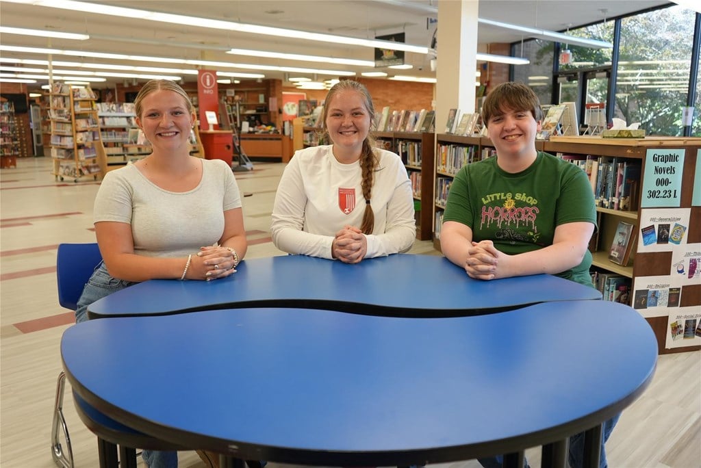 The three WAHS school board reps sit at a table in the library, posing for a photo.